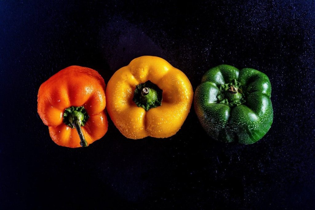 A red, yesslo, and green bell pepper on a black background.